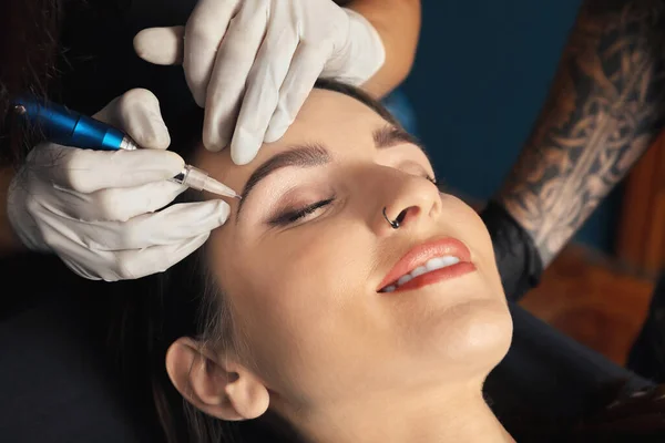 专业纹身画家在美容院的女性脸上涂永久化妆品 — 图库照片