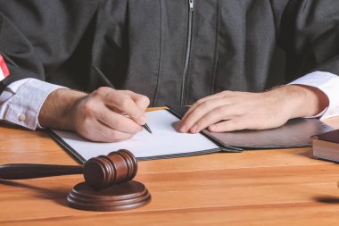Erkek yargıç masadaki belgeleri imzalıyor, yakın plan.