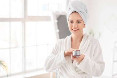 Güzel genç bir kadın banyoya krem sürüyor.