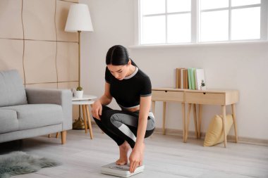 Evde kilosunu ölçen genç bir kadın.