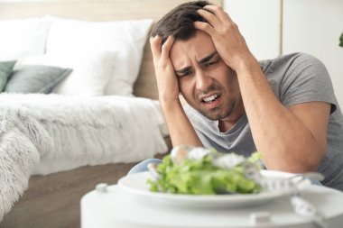Evinde salata ve iştahsızlık çeken genç bir adam.