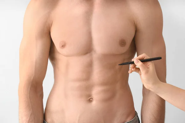 Plastic surgeon applying marking on man\'s body against light background