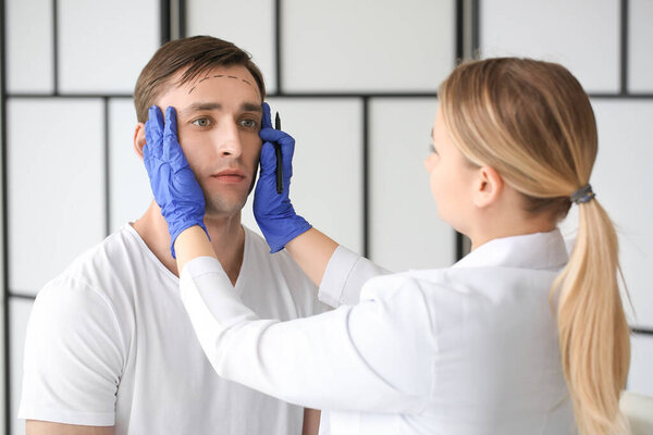Plastic surgeon applying marks on man's face in clinic
