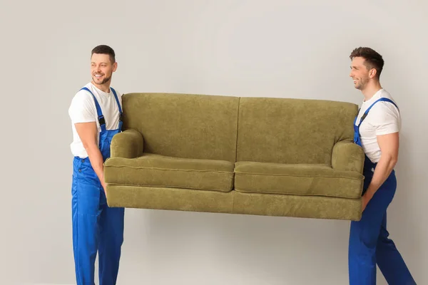 Loaders carrying furniture against grey wall