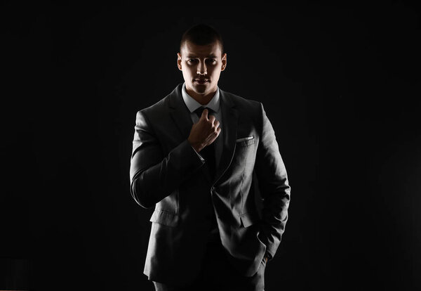 Silhouette of handsome young man in elegant suit on dark background