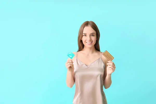 避妊薬とコンドームを持つ若い女性の色の背景 — ストック写真