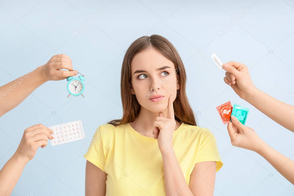 Thoughtful young woman and hands with different means of contraception on color background