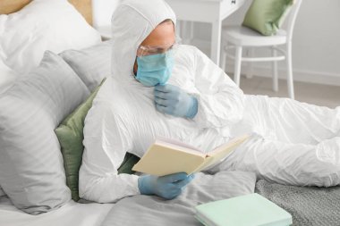 Biyolojik tehlike kıyafetli bir adam evde kitap okuyor.