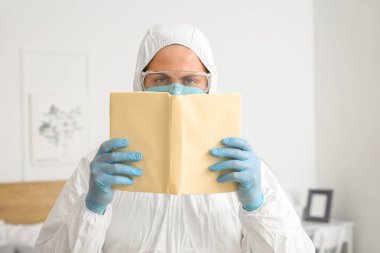 Biyolojik tehlike kıyafetli bir adam evde kitap okuyor.