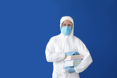 Biyolojik tehlike kıyafeti giymiş ve geçmişiyle ilgili kitapları olan bir adam.