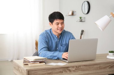 Evde dizüstü bilgisayarda çalışan genç Asyalı adam.