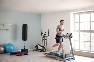 Genç adam spor salonunda koşu bandında antrenman yapıyor.