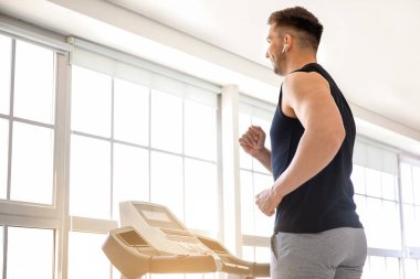 Genç adam spor salonunda koşu bandında antrenman yapıyor.