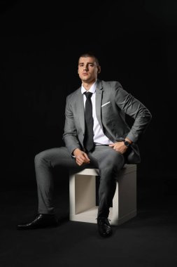 Siyah arka planda zarif takım elbiseli yakışıklı bir genç.