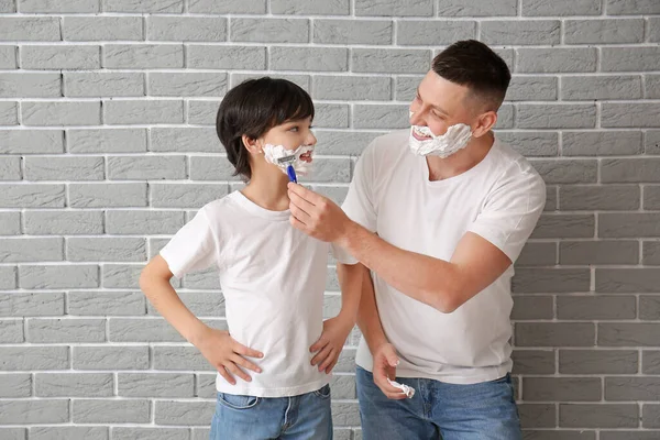 Father and little son shaving on brick background