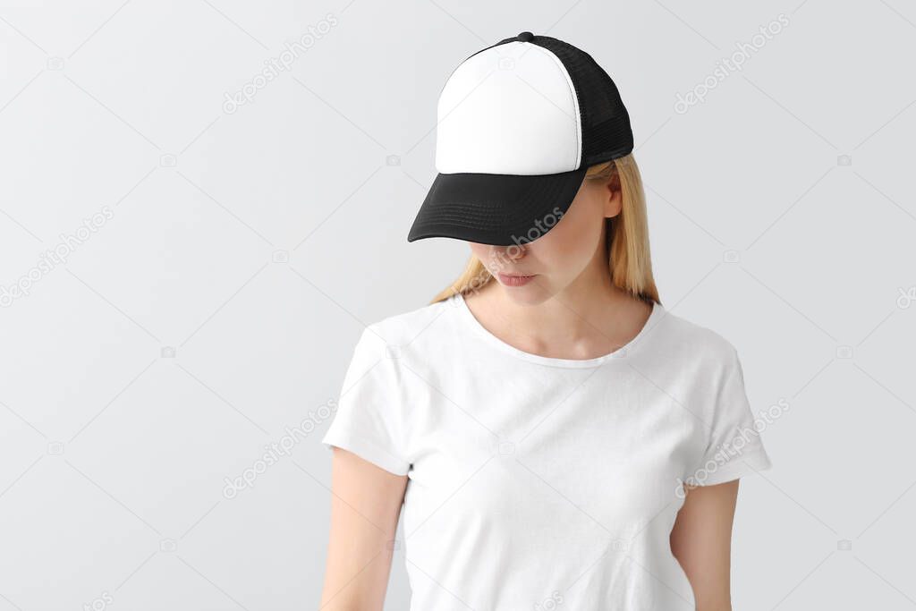 Beautiful young woman in stylish cap on light background