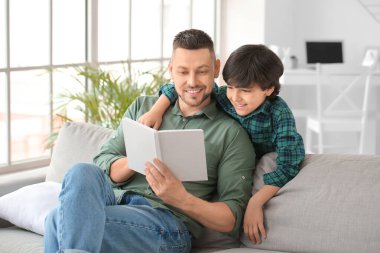 Baba ve küçük oğlu evde kitap okuyor.