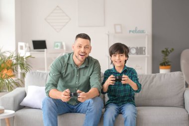 Baba ve küçük oğlu evde video oyunu oynuyorlar.
