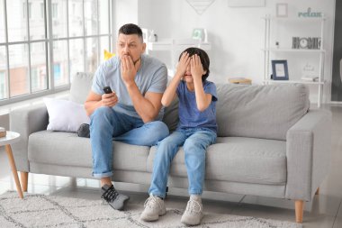 Baba ve küçük oğlu evde televizyon seyrediyor.