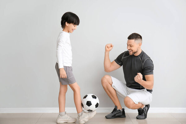 Father and little son with soccer ball near grey wall