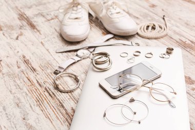 Beyaz ahşap arka planda dizüstü bilgisayarı ve cep telefonu olan kadın aksesuarları