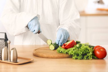 Mutfakta biyolojik tehlike kıyafeti giymiş bir kadın yemek pişiriyor.