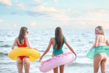 Kumsalda yüzme yüzükleri olan güzel genç kadınlar.