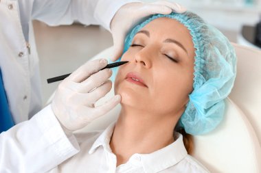 Plastik cerrah klinikte kadının yüzüne izler sürüyor.