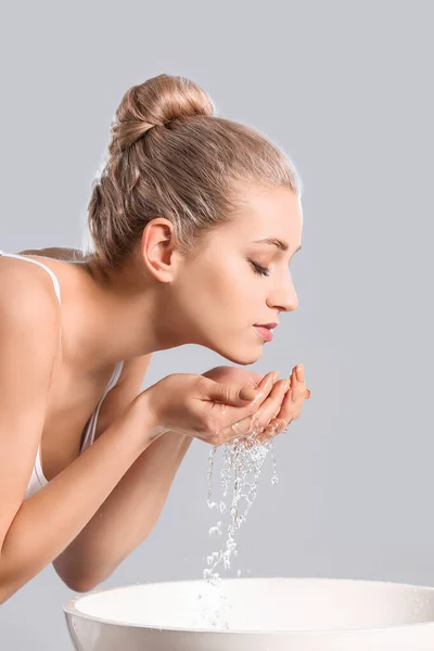 Woman washing face against grey background