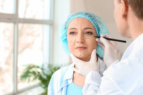 Plastic surgeon applying marks on woman\'s face in clinic