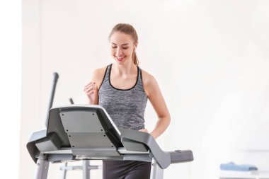 Spor salonundaki koşu bandında antrenman yapan genç bir kadın.