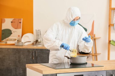 Mutfakta biyolojik tehlike kıyafeti giymiş bir kadın yemek pişiriyor.
