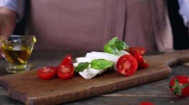 Kadın mozzarella peynirinin üzerine domates ve fesleğenli zeytin yağı döküyor.
