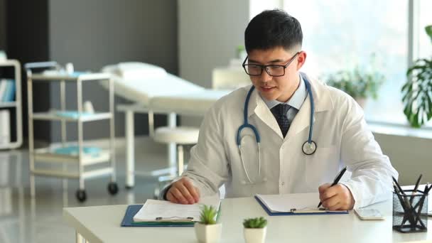 Ασιάτης Γιατρός Που Εργάζεται Στο Τραπέζι Στην Κλινική — Αρχείο Βίντεο