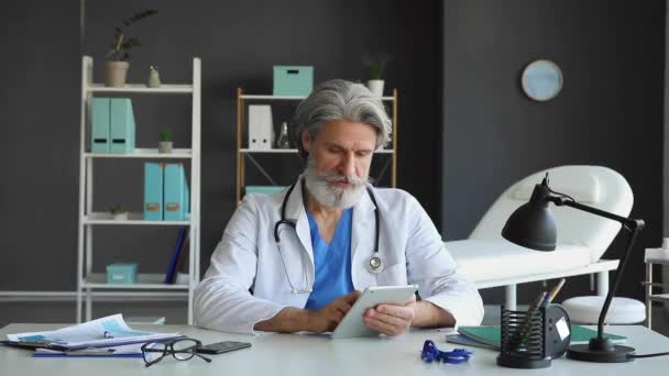 Άρρεν Ανώτερος Γιατρός Χρησιμοποιώντας Tablet Υπολογιστή Στο Τραπέζι Στην Κλινική — Αρχείο Βίντεο