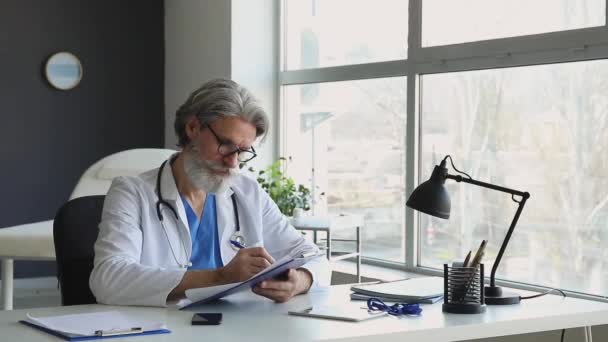Άντρας Ανώτερος Γιατρός Που Εργάζεται Έγγραφα Στο Τραπέζι Στην Κλινική — Αρχείο Βίντεο
