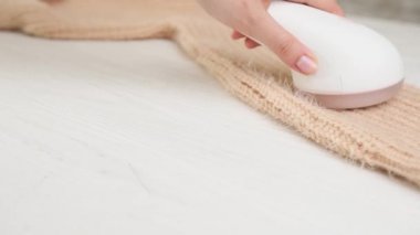Kumaş traş makinesi ve temizlik aleti kullanarak örgü örülmüş süveterin üzerindeki hapları çıkaran kadın.