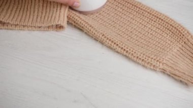 Kumaş traş makinesi ve temizlik aleti kullanarak örgü örülmüş süveterin üzerindeki hapları çıkaran kadın.