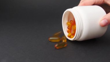 Koyu arka planda balık yağı kapsüllerini dağıtan kadın.