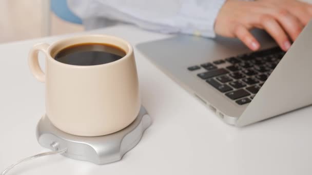 オフィスでラップトップで作業している若い女性のテーブルの上にヒーター付きコーヒーカップ — ストック動画