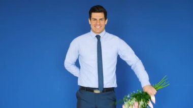 Çiçek buketi olan yakışıklı bir beyefendi ve renk arka planına karşı hediye olarak izleyiciyi selamlıyor.