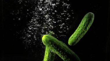 Karanlık arka planda suya düşen taze salatalıklar.