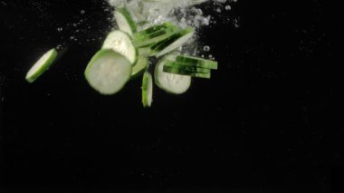 Taze salatalık dilimleri koyu arkaplana karşı suya düşer.