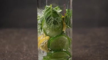 Gri arka planda salatalık, limon ve nane ile bardağa su dökülüyor. Yakın plan.