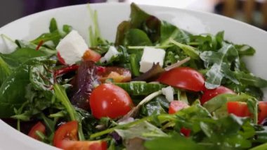 Lezzetli peynir parçaları sebze salatasıyla kaseye düşüyor, yakın plan.