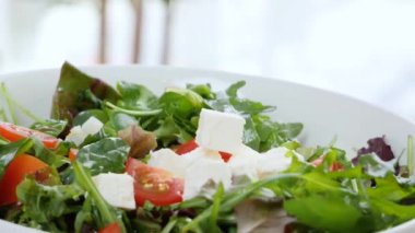 Lezzetli peynir parçaları sebze salatasıyla kaseye düşüyor, yakın plan.