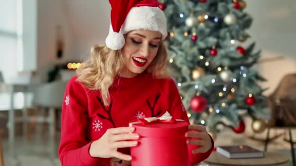 Красива Молода Жінка Капелюсі Санта Відкриває Різдвяний Подарунок Вдома — стокове відео