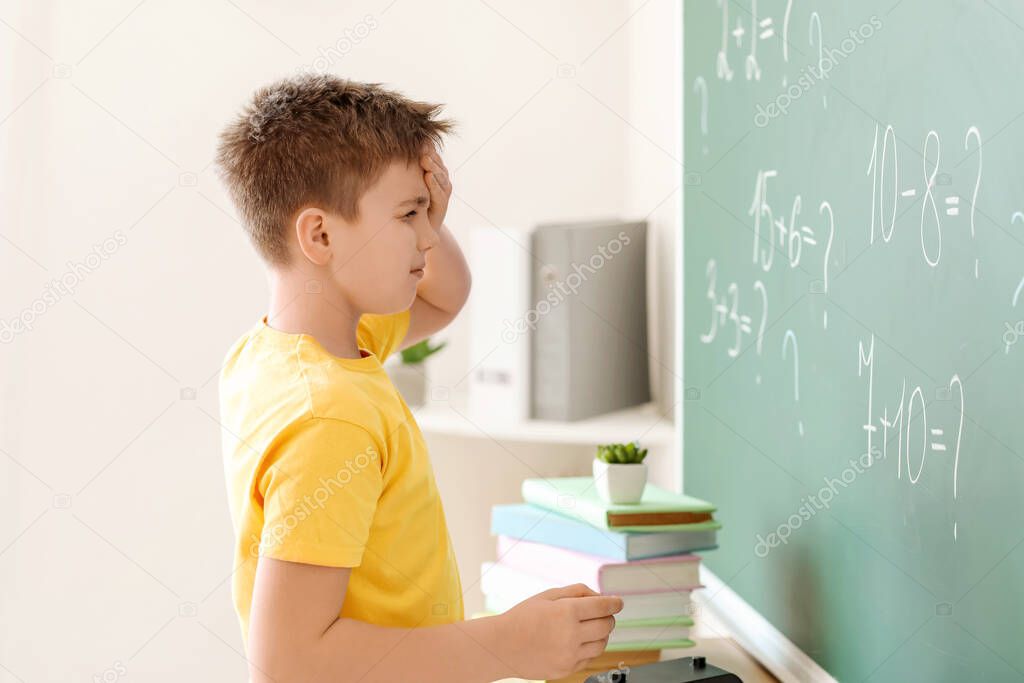 Troubled little boy near school blackboard in classroom