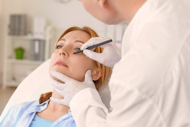 Plastik cerrah klinikte kadının yüzüne izler sürüyor.