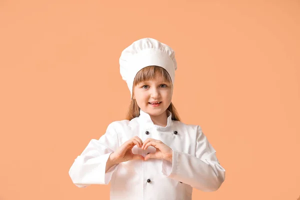 Cute little chef making heart with her hands on color background